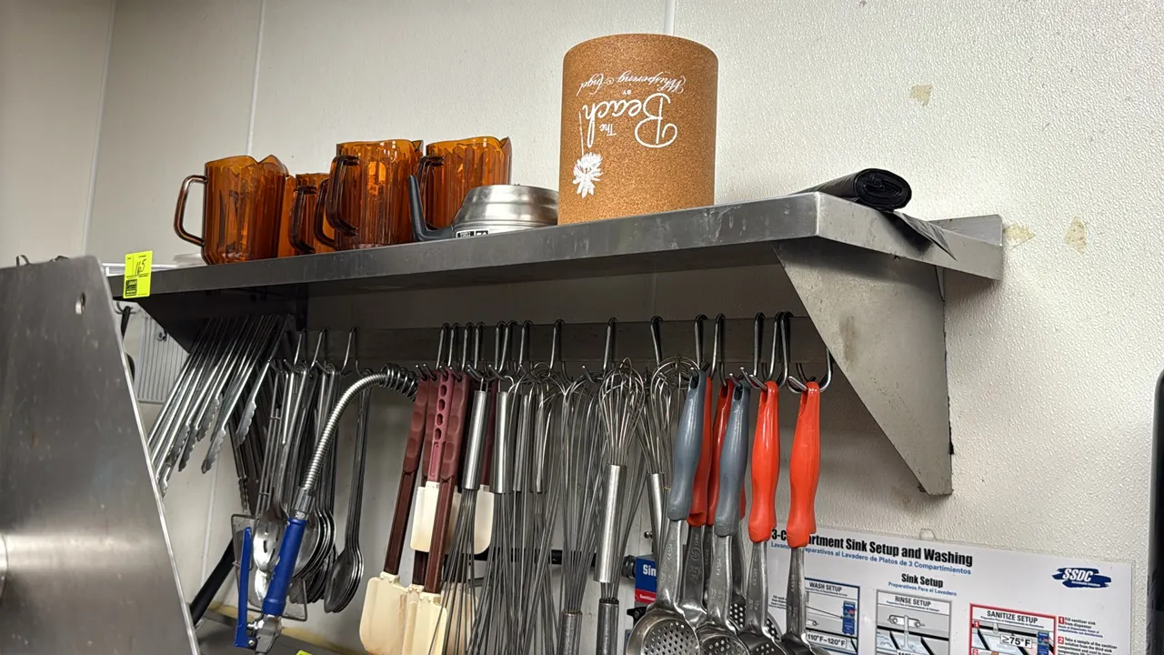 Stainless steel wall shelf with pot rack. Features stainless steel construction, an integrated hanging bar with hooks, and heavy-duty wall mounting br
