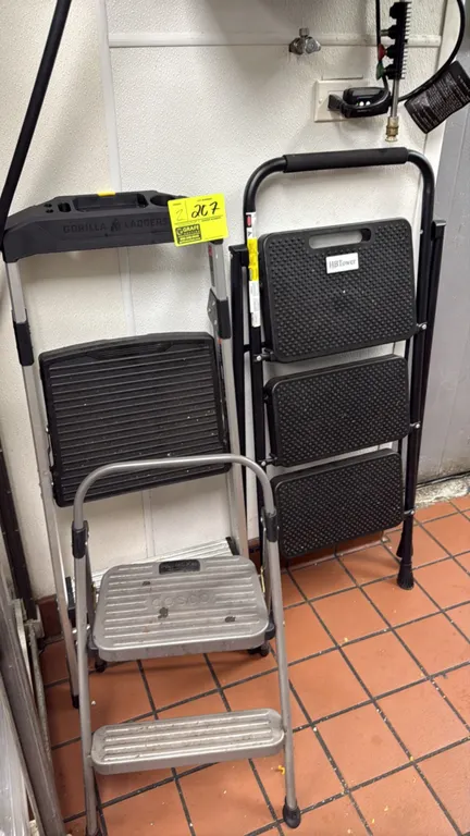 Assorted metal folding step stools. Includes Gorilla Ladders step stool with top project tray, HBTower 3-step folding stool with padded hand grip, and