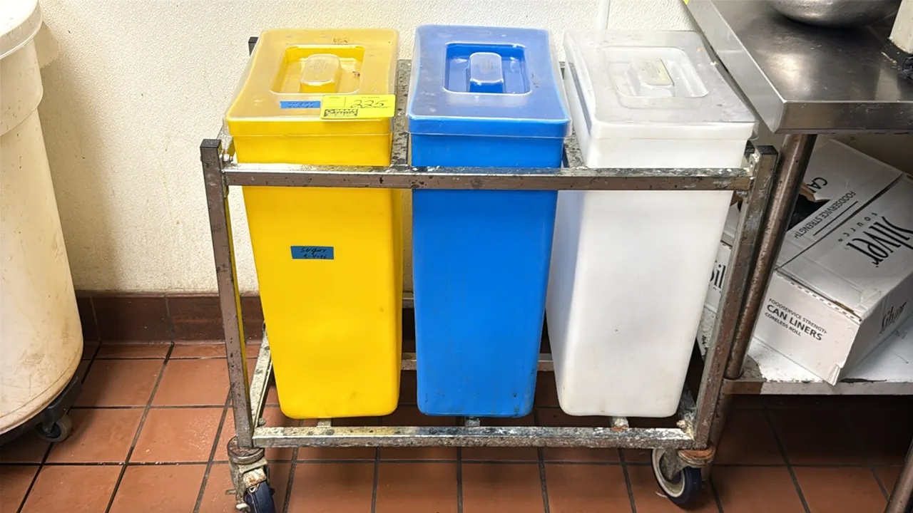 Mobile 3-bin ingredient rack. Includes (3) plastic ingredient bins with clear lids in yellow, blue, and white. Mounted on a metal frame with swivel ca