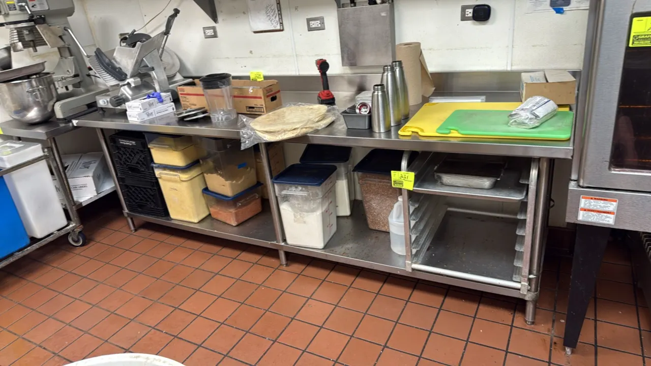 Stainless steel work table. Features a rear backsplash and undershelf. 108"L x 30"W. Mounted on six tubular legs with adjustable bullet feet. Contents