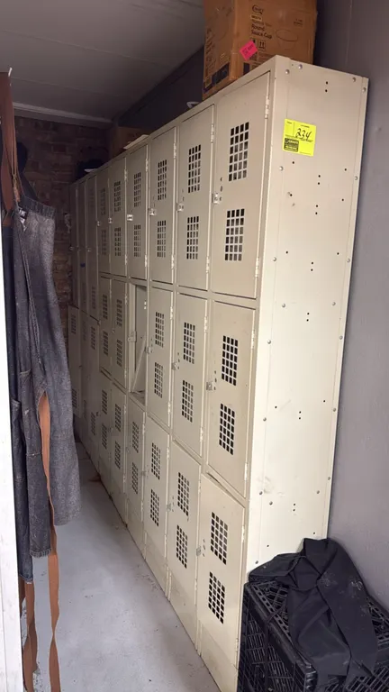 Metal employee locker bank. Features (9) 3-tier sections with ventilated metal doors and padlock hasps, providing 27 total locker compartments. Tan pa