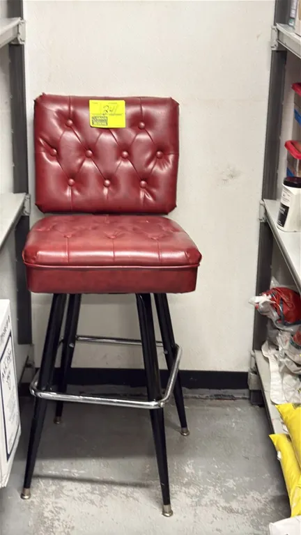 Bar height swivel chair. Features burgundy button-tufted vinyl upholstery on a padded seat and backrest. Mounted on black metal tapered legs with a ch