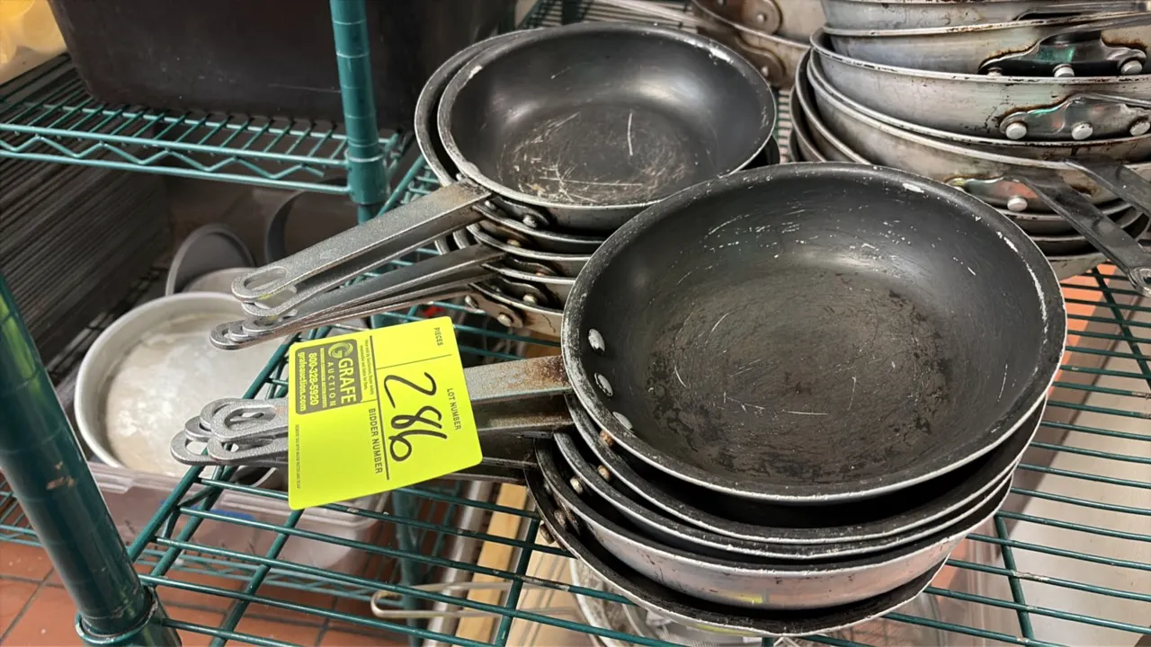 Assorted commercial aluminum fry pans. Includes various sizes with riveted handles and non-stick or bare metal interiors. Shelving not included.