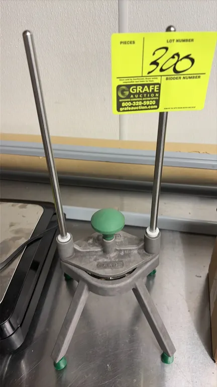 Garde manual fruit wedger. Features cast aluminum construction, dual vertical guide rods, and green push knob. Mounted on angled legs with rubber feet