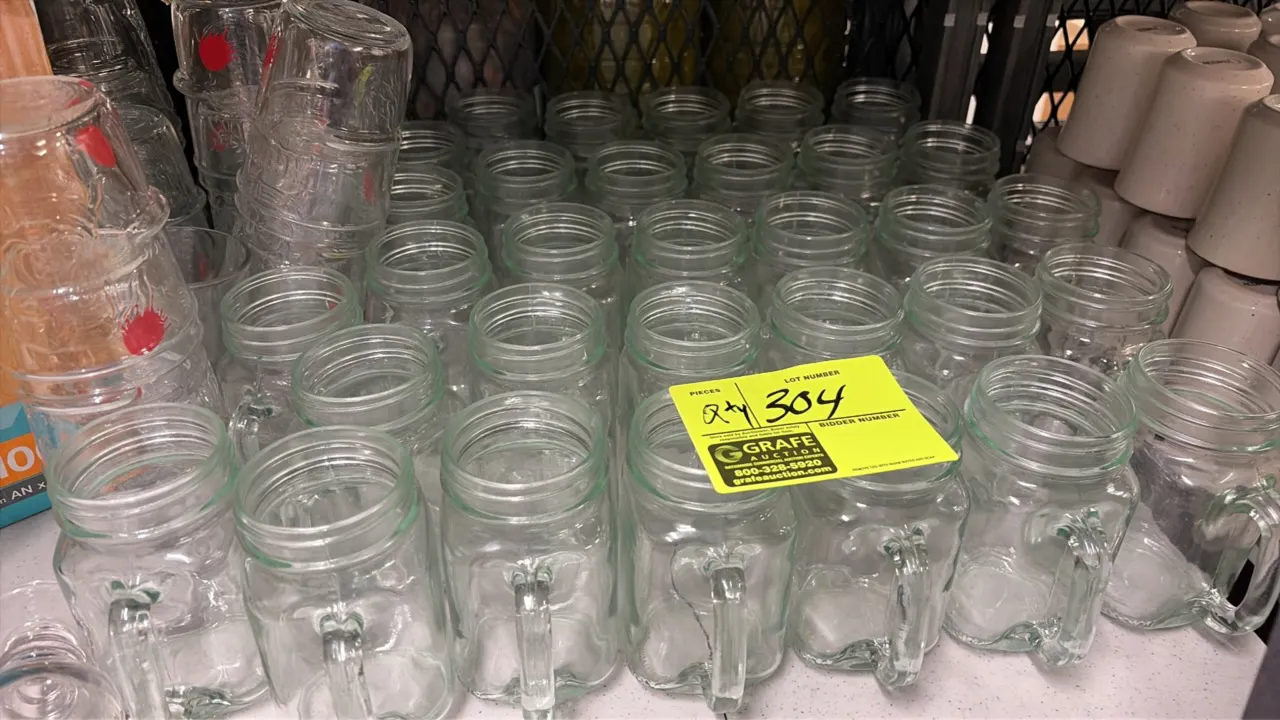 Glass mason jar mugs. Features clear molded glass construction, integrated side handles, and threaded rims. Surrounding glassware not included.