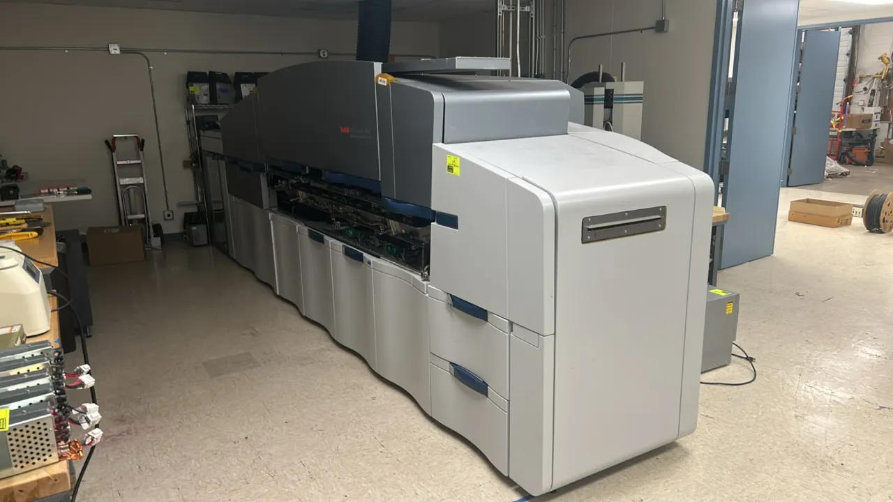 Kodak NexPress 2100 digital production color press. Features 5-color print engine, sheet-fed feeder unit with dual drawers, and high-capacity stacker