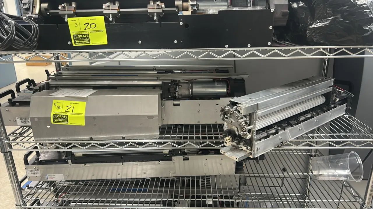 Kodak NexPress 2100 digital production press components. Features roller assemblies, internal drive motors, and metal housing frames. Wire shelving no