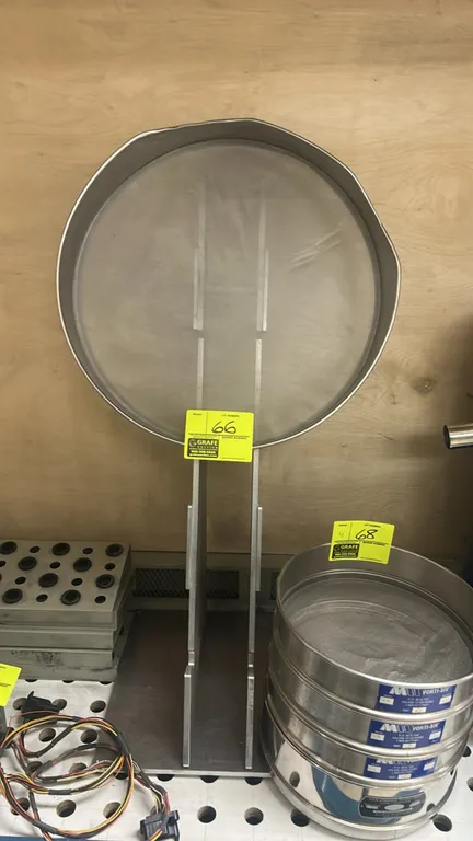 Round metal industrial sieve with slotted metal stand. Features fine wire mesh screen. Note: Sieve rim is bent. Surrounding items not included.