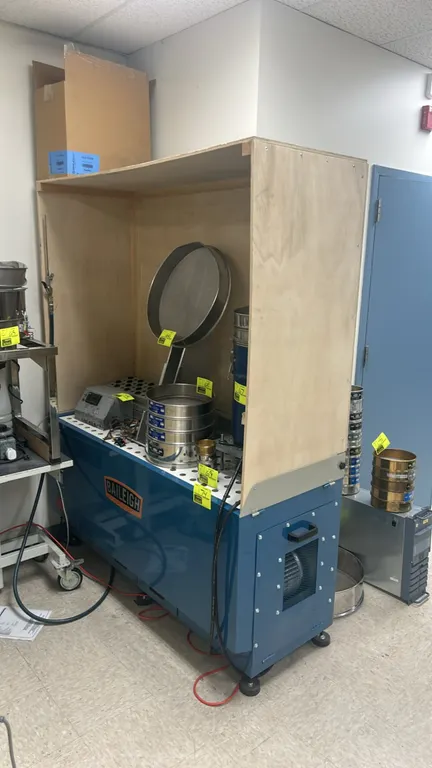 Baileigh cabinet base with custom wooden containment hood. Features perforated metal top surface and integrated side exhaust blower. 62" x 24". Mounte