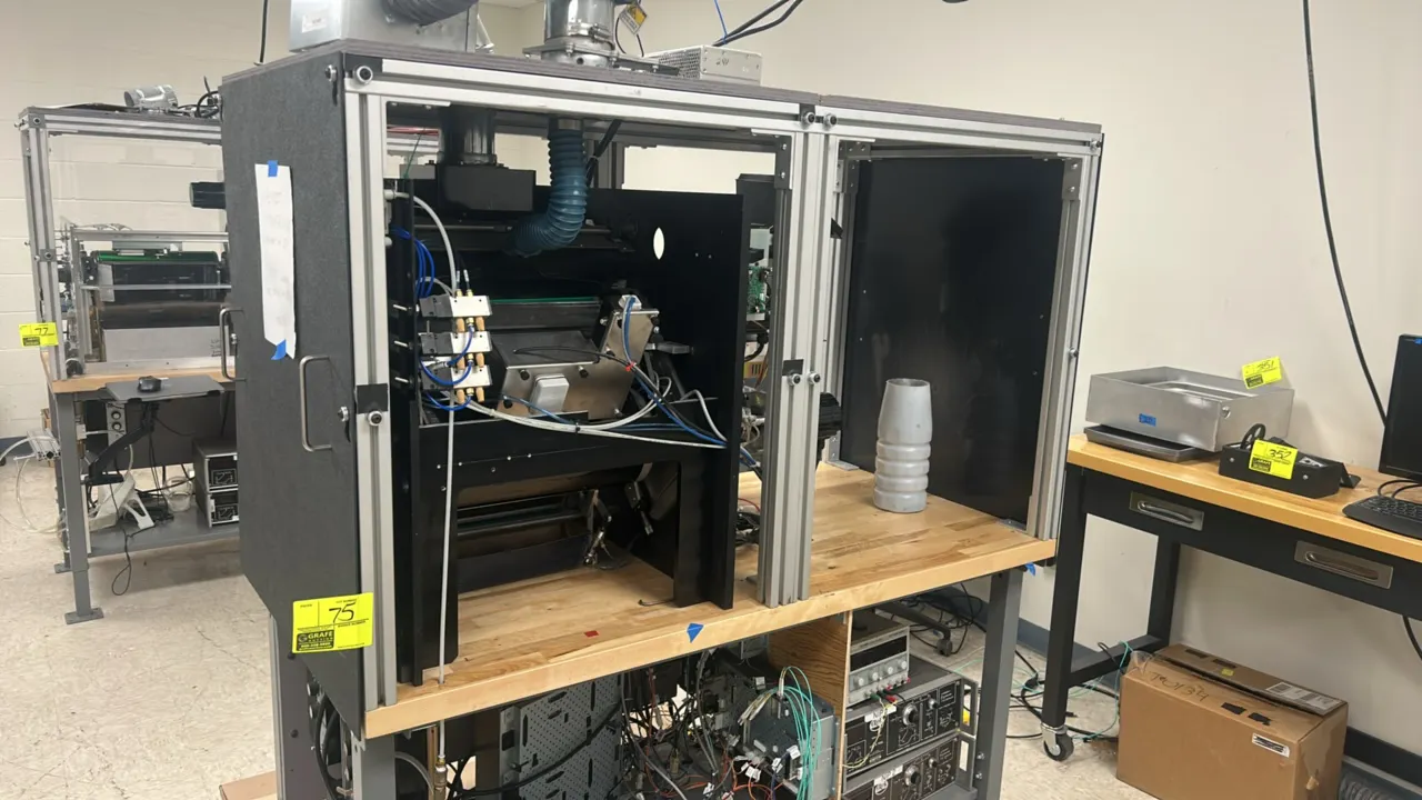 Custom industrial test bench apparatus. Features an aluminum extrusion frame enclosure, wood work surface, exhaust ducting, and lower shelf with integ