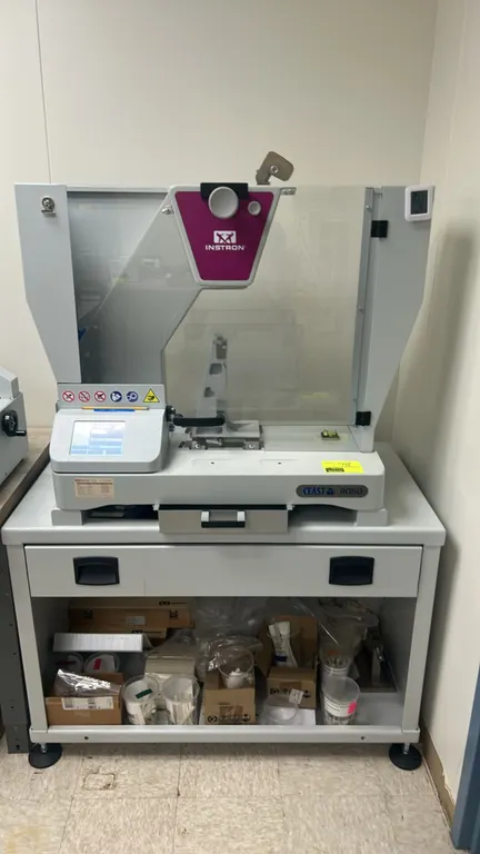 Instron CEAST 9050 motorized pendulum impact tester. Features digital touchscreen display, transparent safety enclosure shield, and specimen collectio