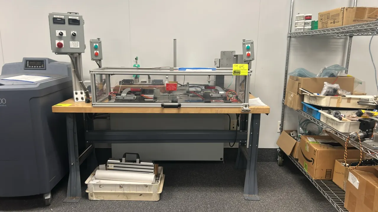 Custom industrial testing and assembly station. Features an extruded aluminum safety enclosure with transparent panels, toggle clamping fixtures, dual