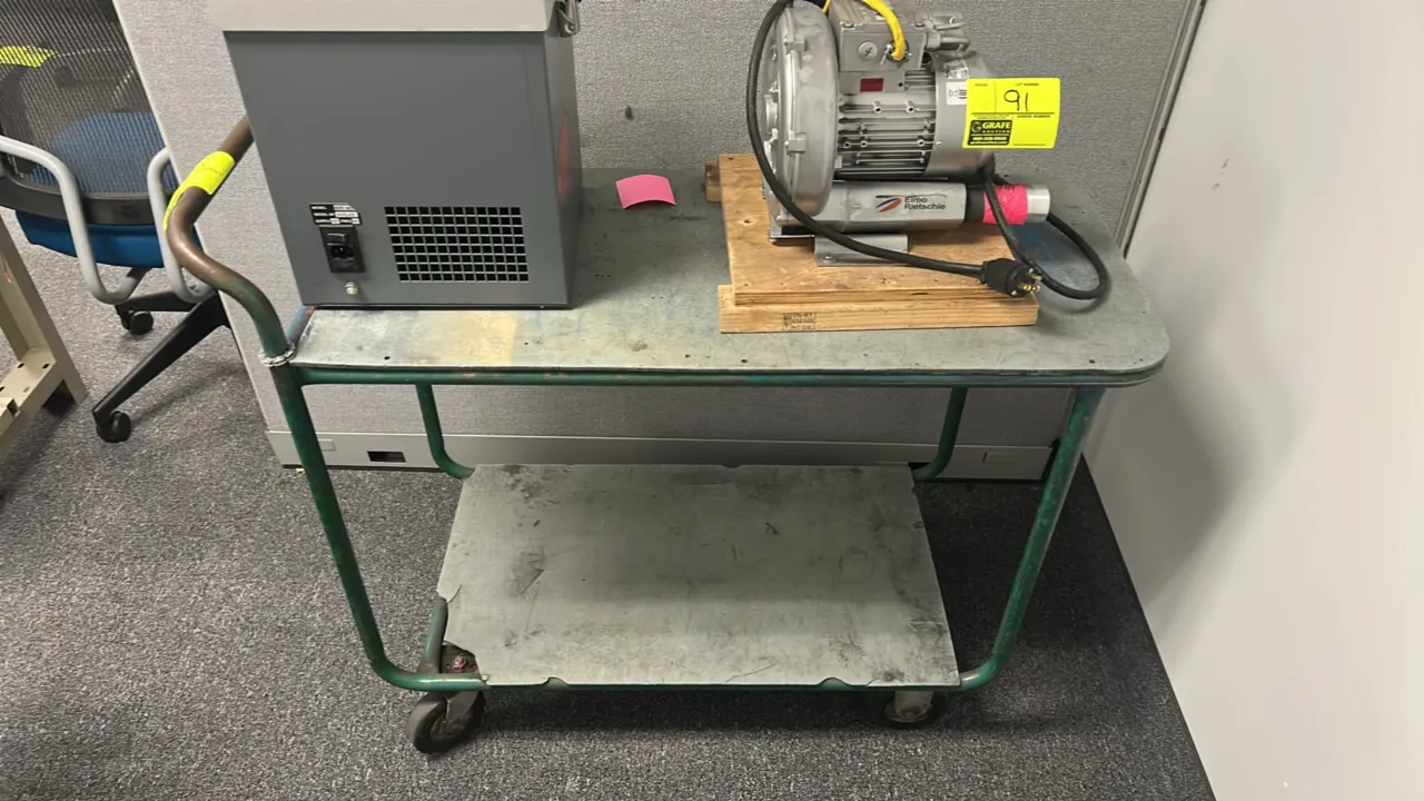 Metal 2-tier utility cart. Features green tubular metal frame, integrated push handle, and two utility shelves. 44"L. Mounted on casters. Contents not