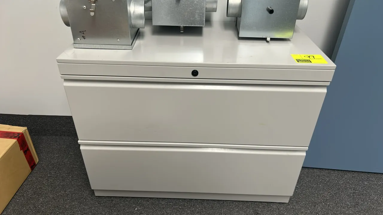 Two-drawer metal lateral file cabinet. Features two wide drawers with integrated full-width pulls and top center lock mechanism. Finished in light gra