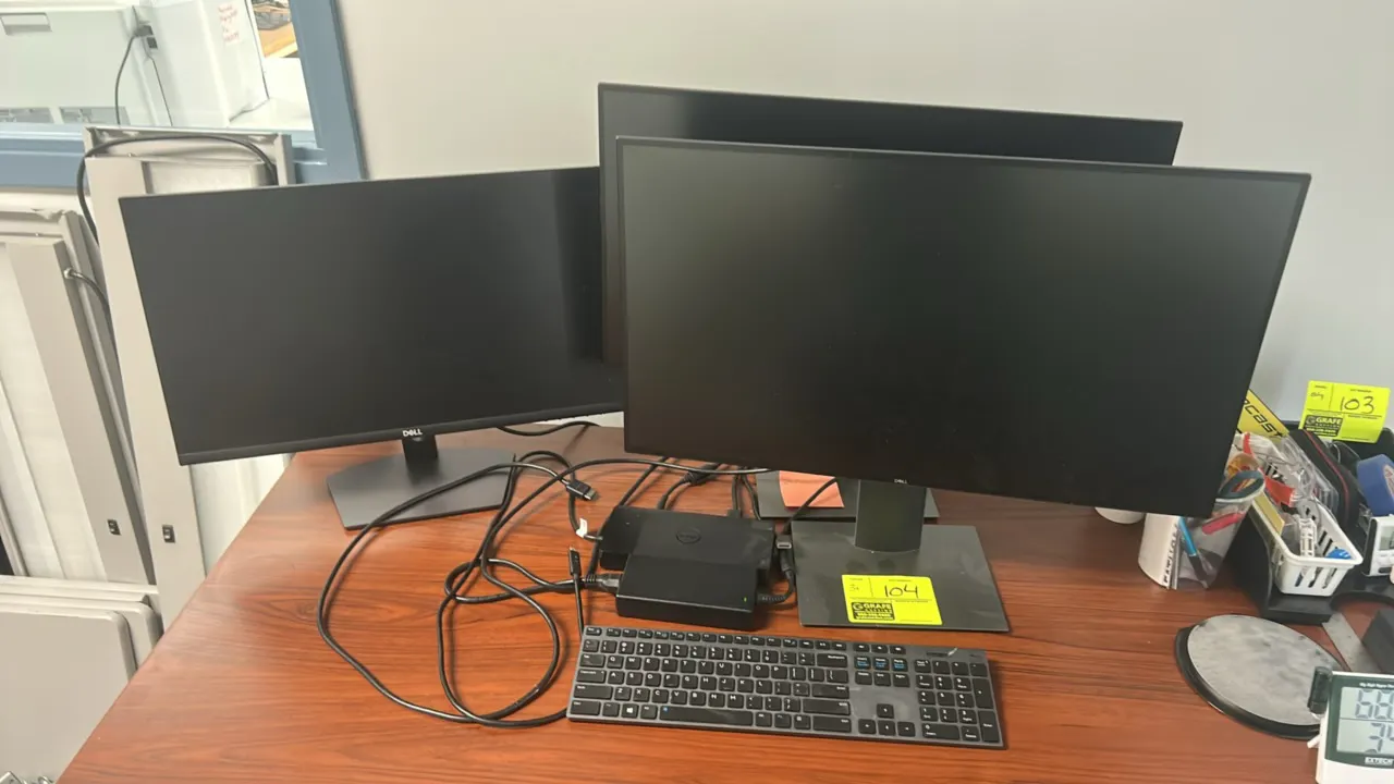 Dell 27" flat panel monitors with desk contents. Includes Dell flat panel monitors on desktop stands, Dell docking station with AC power adapter, Dell
