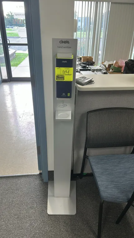 Cintas automatic hand sanitizer dispenser. Features touchless automatic dispensing and an integrated drip tray. Mounted on a freestanding silver-tone