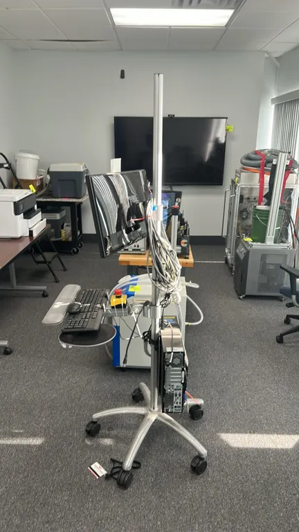 Mobile computer workstation. Includes 24" ASUS monitor, HP ProDesk SFF PC, keyboard, mouse, and wrist rest. Features emergency stop switch and cord ma
