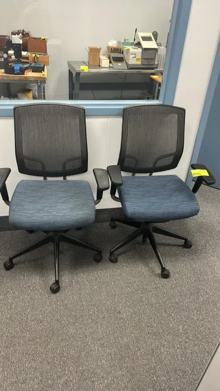 Rolling office chairs. Features black mesh backs, blue patterned fabric upholstered cushioned seats, and armrests. Mounted on 5-star bases with caster