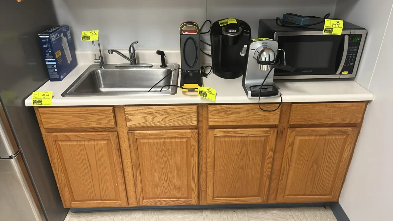 Breakroom cabinet ensemble with countertop and sink. Features upper and lower woodgrain laminate cabinets, white laminate countertop, and single-basin