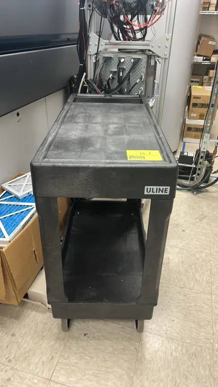 ULINE 2-tier poly utility cart. Features a molded push handle with integrated storage tray, lipped top shelf, and deep bottom shelf. 3'L. Mounted on c