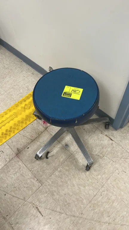 Pneumatic rolling stool. Features a round blue padded swivel seat with height adjustment lever. Mounted on a 5-star metal base with casters. Note: Sea