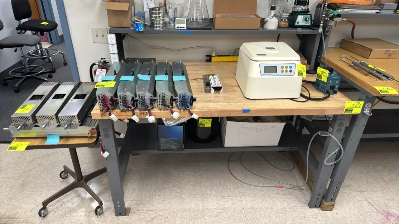 Adjustable-height laboratory work table. Features a wood butcher block style top, upper shelf riser, and lower shelf. 6' x 3'. Supported by adjustable