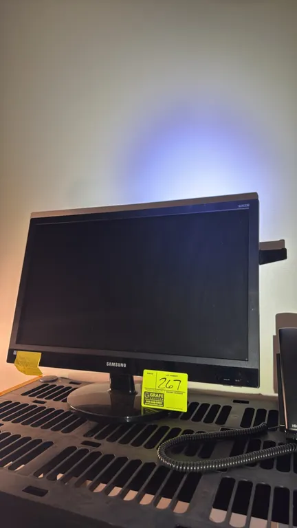 Samsung S27C230 27" computer monitor. Features widescreen display and black finish. Mounted on a desktop stand. Telephone and shelving not included.