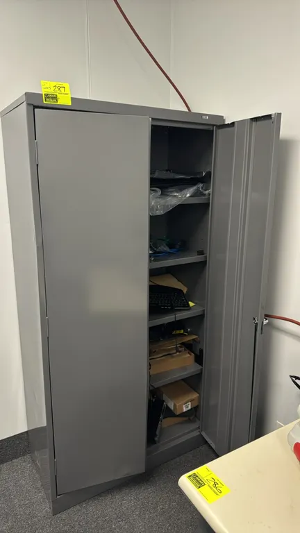 Uline 2-door metal storage cabinet with contents. Features 4 interior shelves and locking latch handle. Includes various computer cables, power cords,