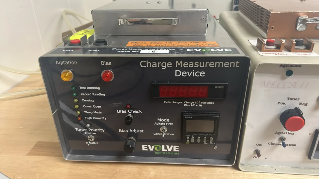 Evolve Additive Solutions charge measurement device. Features a top test chamber with handle, front-panel digital readout, integrated Omron digital ti