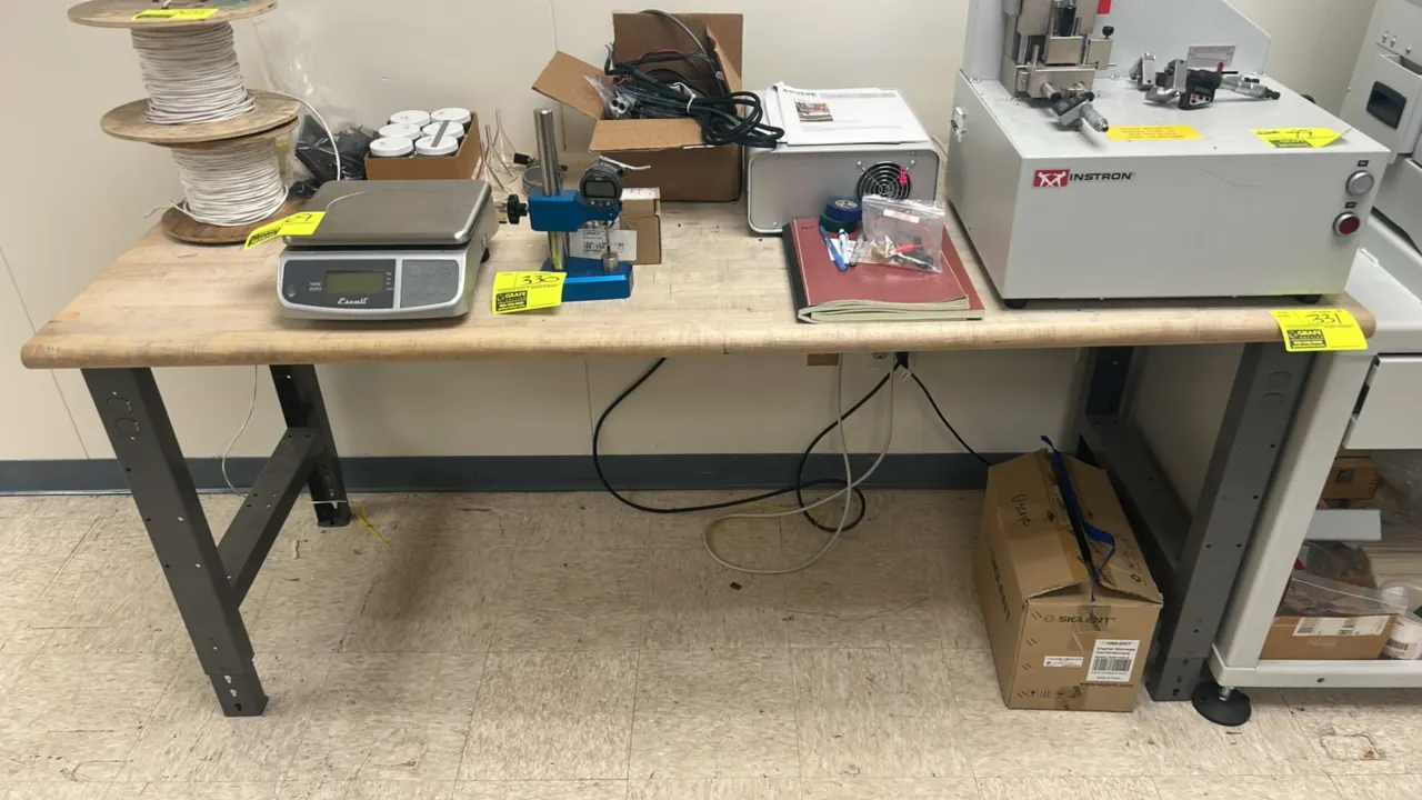 Industrial workbench table. Features a laminated wood butcher block top. 72" x 30". Mounted on a gray metal base with adjustable-height legs. Contents