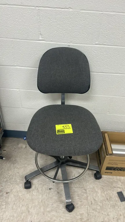 Upholstered rolling drafting office chair. Features gray fabric cushioned seat and back, armless design, and circular chrome footrest ring. Mounted on
