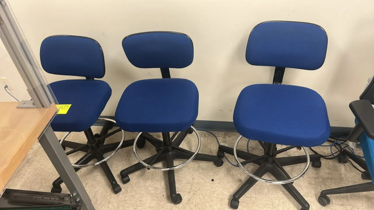 Cushioned rolling drafting office chairs. Features blue fabric upholstery, cushioned seats and backrests, armless design, and chrome footrest rings. M