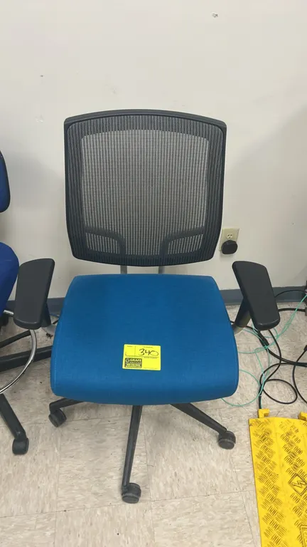 Office task chair. Features a black mesh back, blue cushioned fabric seat, and adjustable armrests. Mounted on a 5-star base with casters.