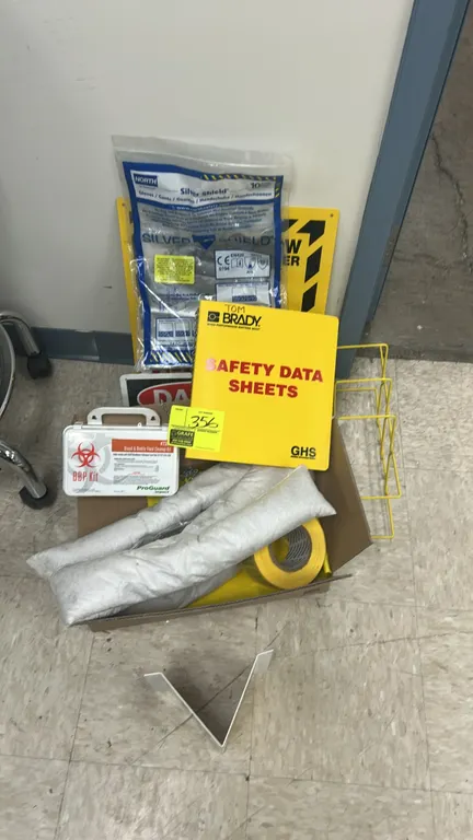 Assorted workplace safety supplies and signage. Includes a Brady GHS Safety Data Sheets binder, Impact ProGuard Blood & Bodily Fluid Cleanup Kit with