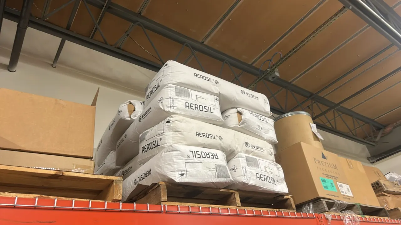 Assortment of industrial chemical powders. Includes Evonik AEROSIL fumed silica bags, AEROXIDE, and boxed materials with remaining contents on wooden