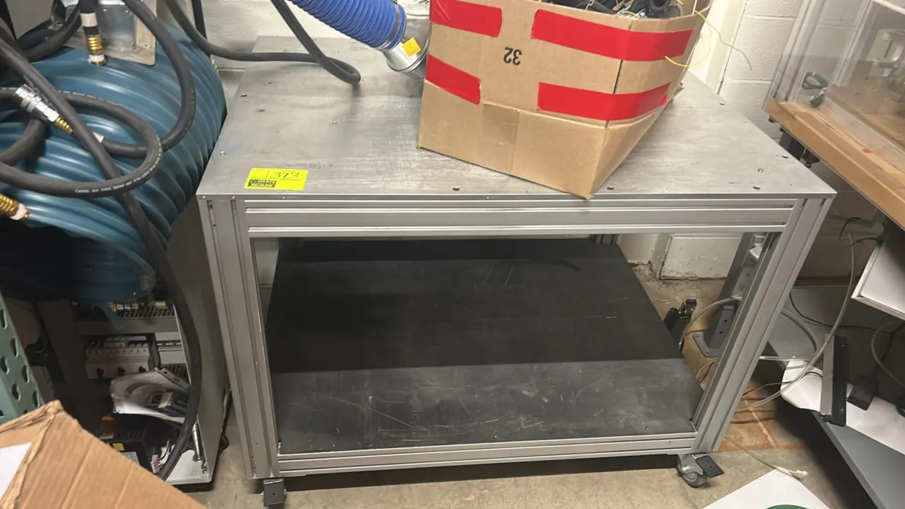 Metal 2-tier cart. Features an extruded aluminum frame, solid metal top surface, and lower shelf. 4' x 3'. Mounted on casters. Note: Contents not incl