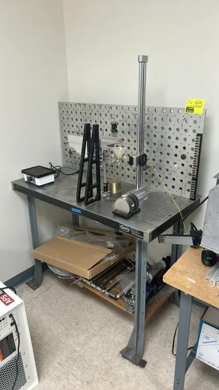 Newport Research Corporation metal workbench with undershelf and quantity of custom industrial machinery. Features threaded grid optical top, perforat