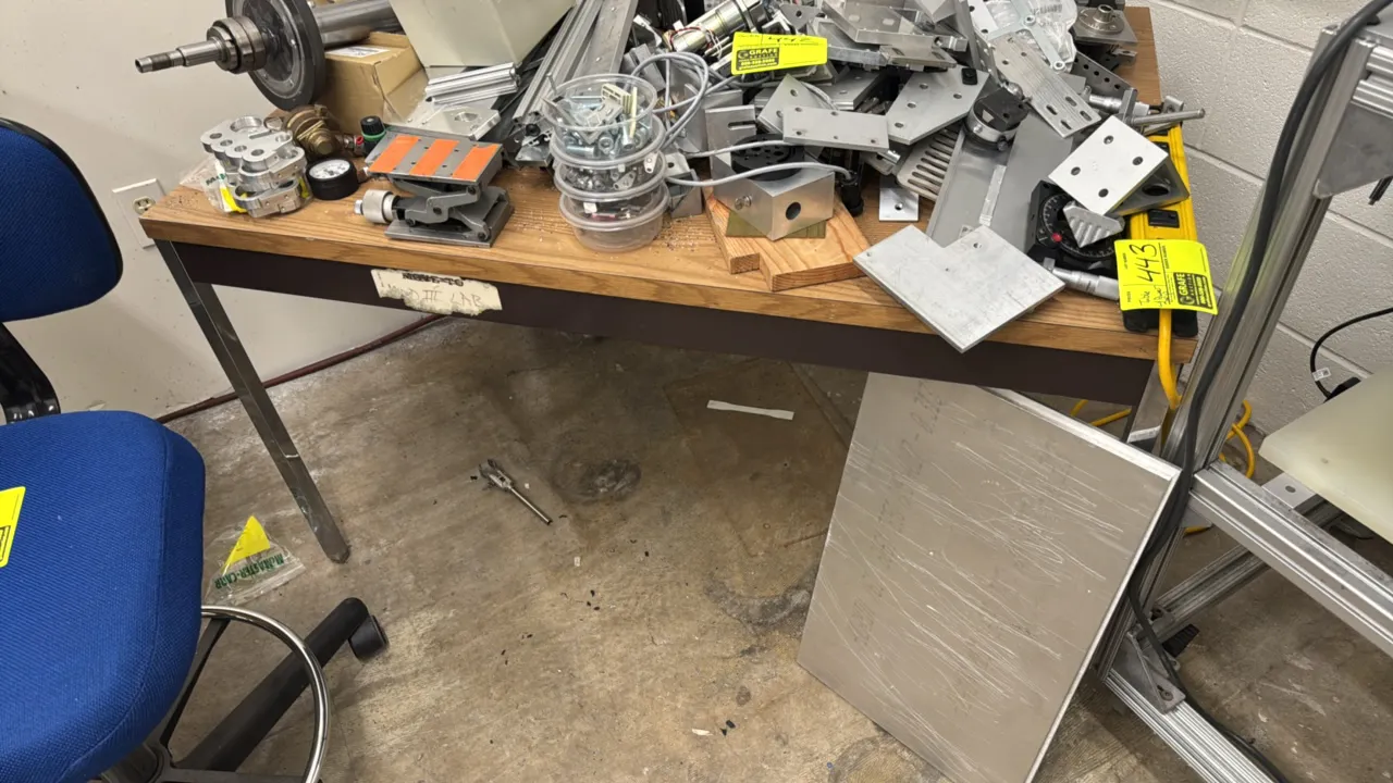 Work table with wood-grain laminate top. Features a dark brown steel frame apron and chrome legs. Dimensions: 44" x 30". Contents not included.