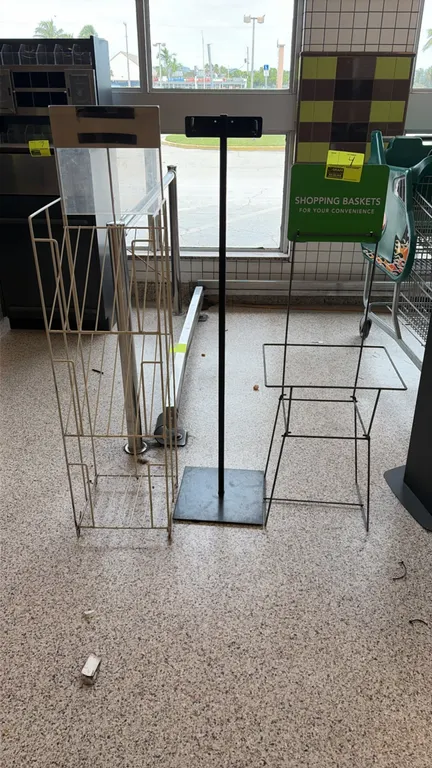 Assorted retail display racks and stands. Includes a white wire literature rack with clear header, a black metal sign stand with flat base, and a blac