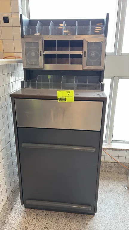 Condiment station with integrated waste receptacle. Features upper organizer hutch with clear acrylic condiment bins, utensil sorting cubbies, dual di