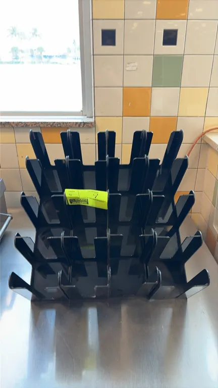 Black acrylic lid holders. Features 4-compartment slotted design with labeled size designations and tiered configuration. Designed for countertop plac