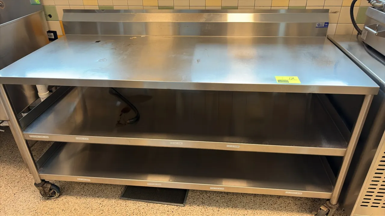 Stainless steel work table. Features an integrated backsplash and double undershelf. 72" x 32". Mounted on casters.