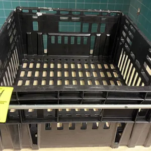 Plastic bread crate. Features molded black plastic construction, slotted sides and bottom, and a metal stacking bail bar.