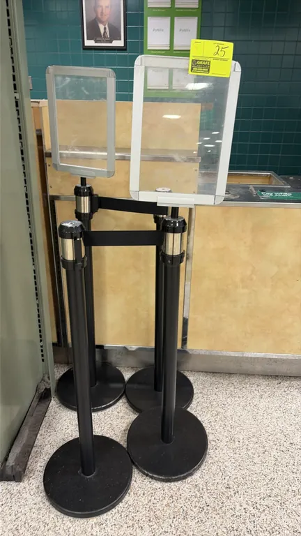 AirFlo retractable belt stanchions. Features black metal posts with circular weighted bases, black retractable belts, and (2) top-mounted sign display