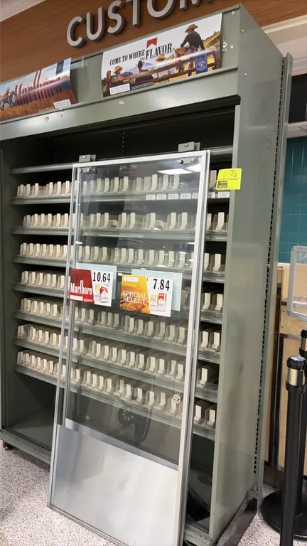 Cigarette display cabinet. Features metal frame construction, multiple shelves with spring-loaded pack pushers, top advertising display header, and sl