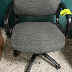 Office chair. Features gray textured fabric upholstery, padded seat and backrest, and fixed black armrests. Mounted on a 5-star swivel base with caste