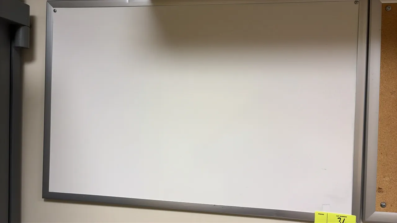 Dry-erase whiteboard. Features an aluminum frame and white writing surface. 3'L. Wall-mounted. Note: Dent along top edge of frame. Adjacent corkboard