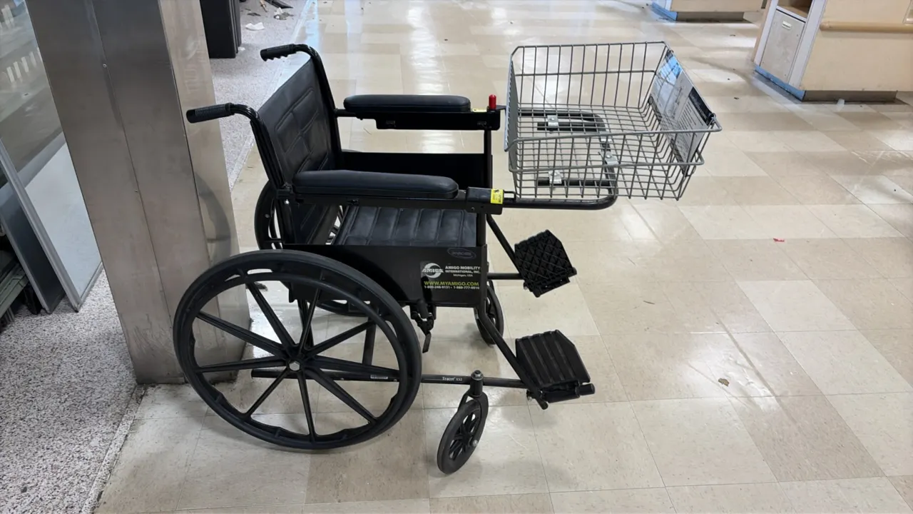 Amigo Mobility manual wheelchair. Features attached front wire shopping basket, black vinyl upholstery, padded armrests, flip-up footrests, rear mag w