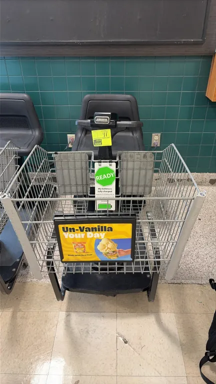 Amigo Value Shopper motorized grocery shopping cart. Features front wire basket with advertisement placard, molded plastic seat, handlebar controls, a