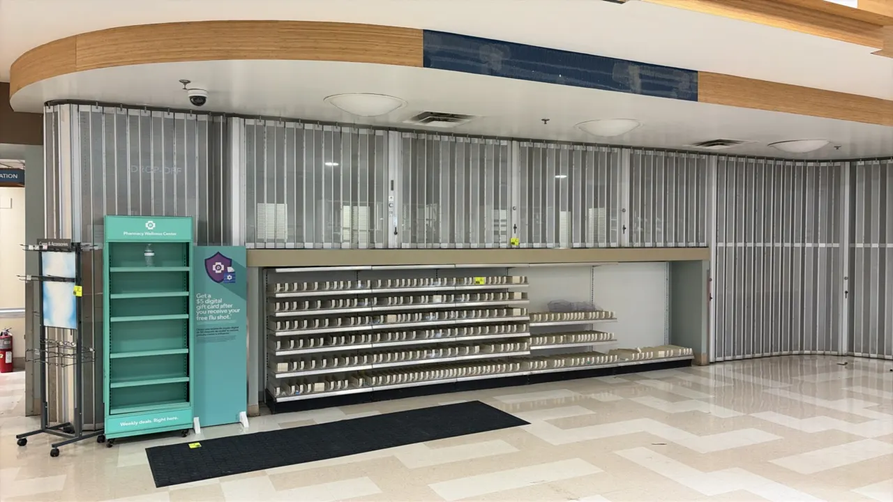 Folding accordion security gate. Features perforated metal panels and ceiling-mounted track system. Keys not included. Shelving, fixtures, and surroun